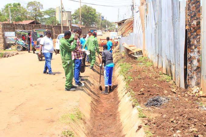 Community members clearing a drainage trench along a local road to help prevent flooding